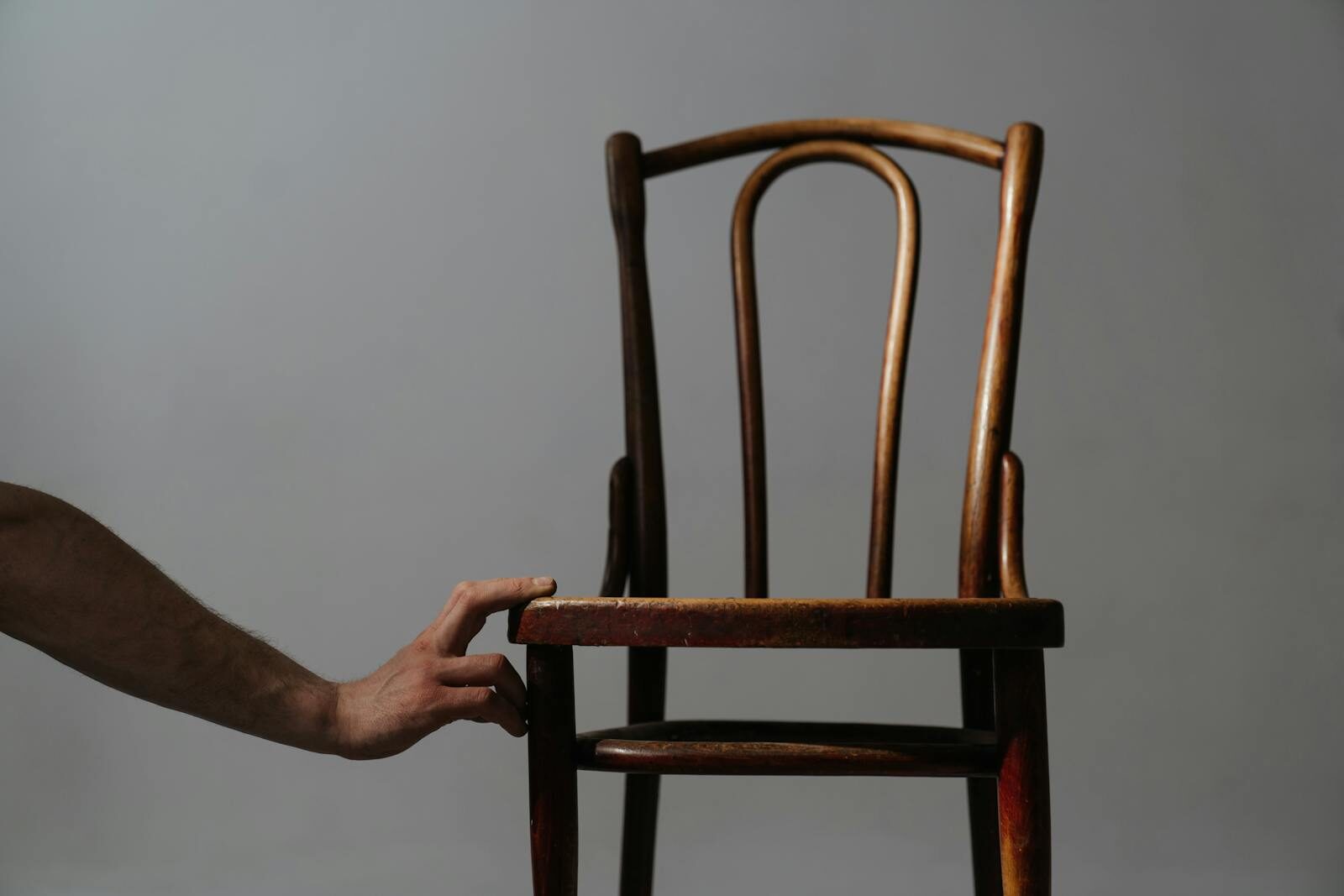 An artistic still life of a classic wooden chair with a hand reaching out, emphasizing minimalist design.