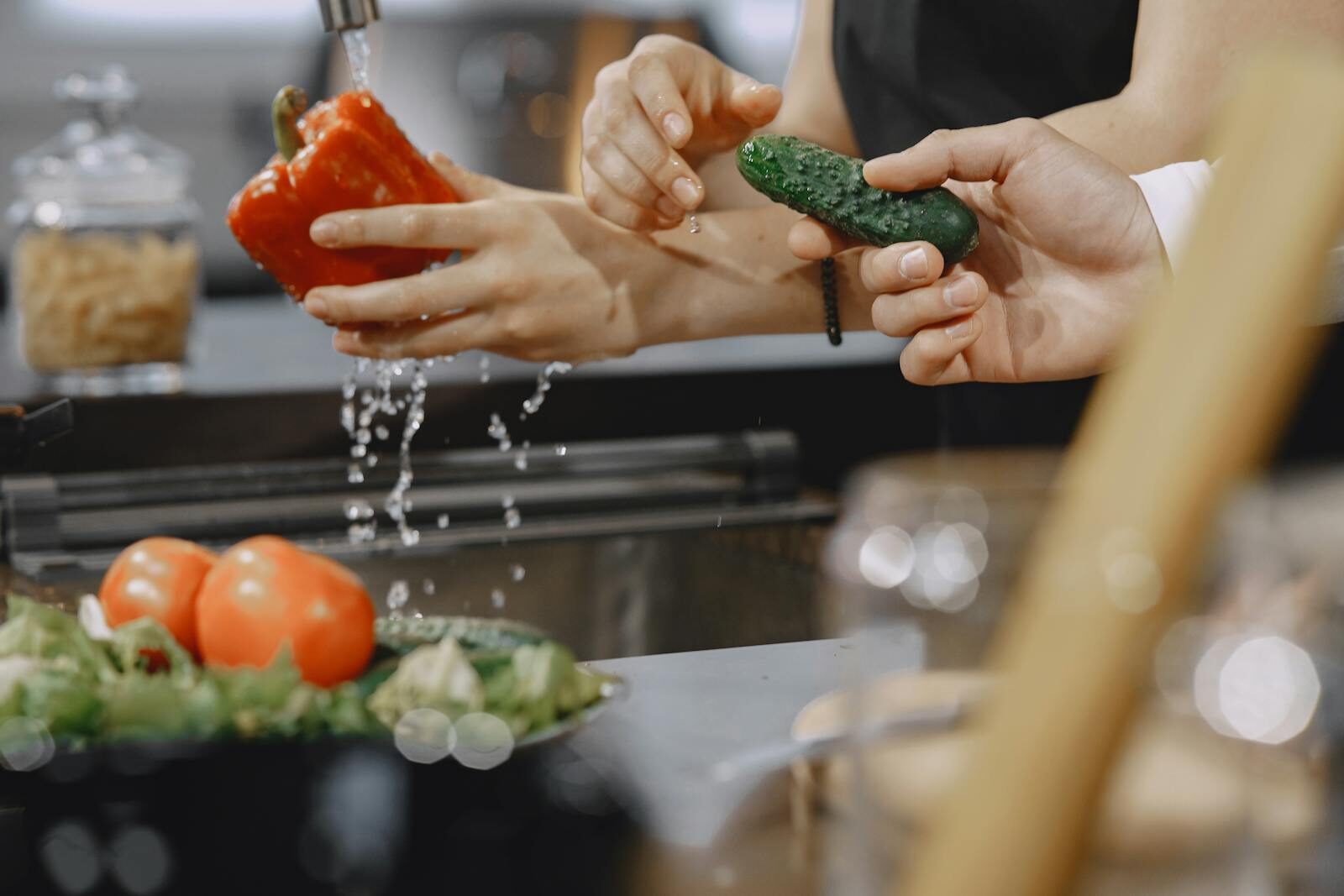 Close-up of hands washing vegetables in a modern kitchen sink.