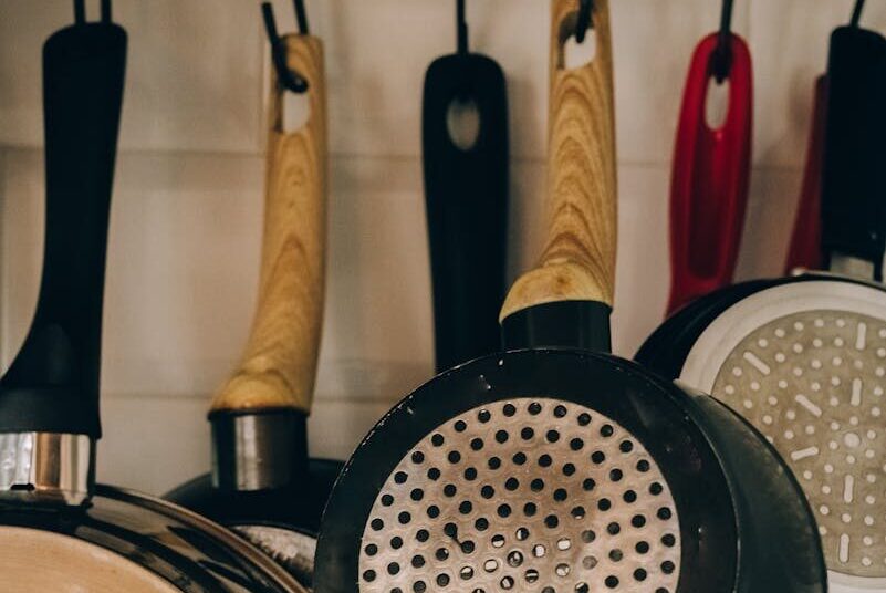 Collection of metal frying pans with wooden and plastic handles hanging on hooks near wall in house