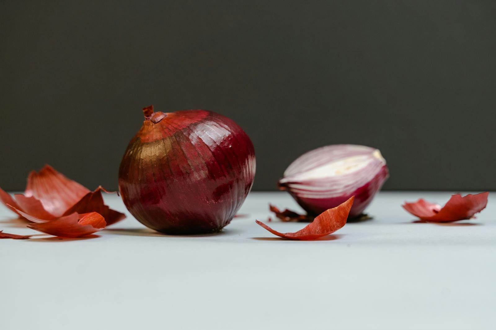 Close-up of whole and sliced red onions with peeled skins on white surface.